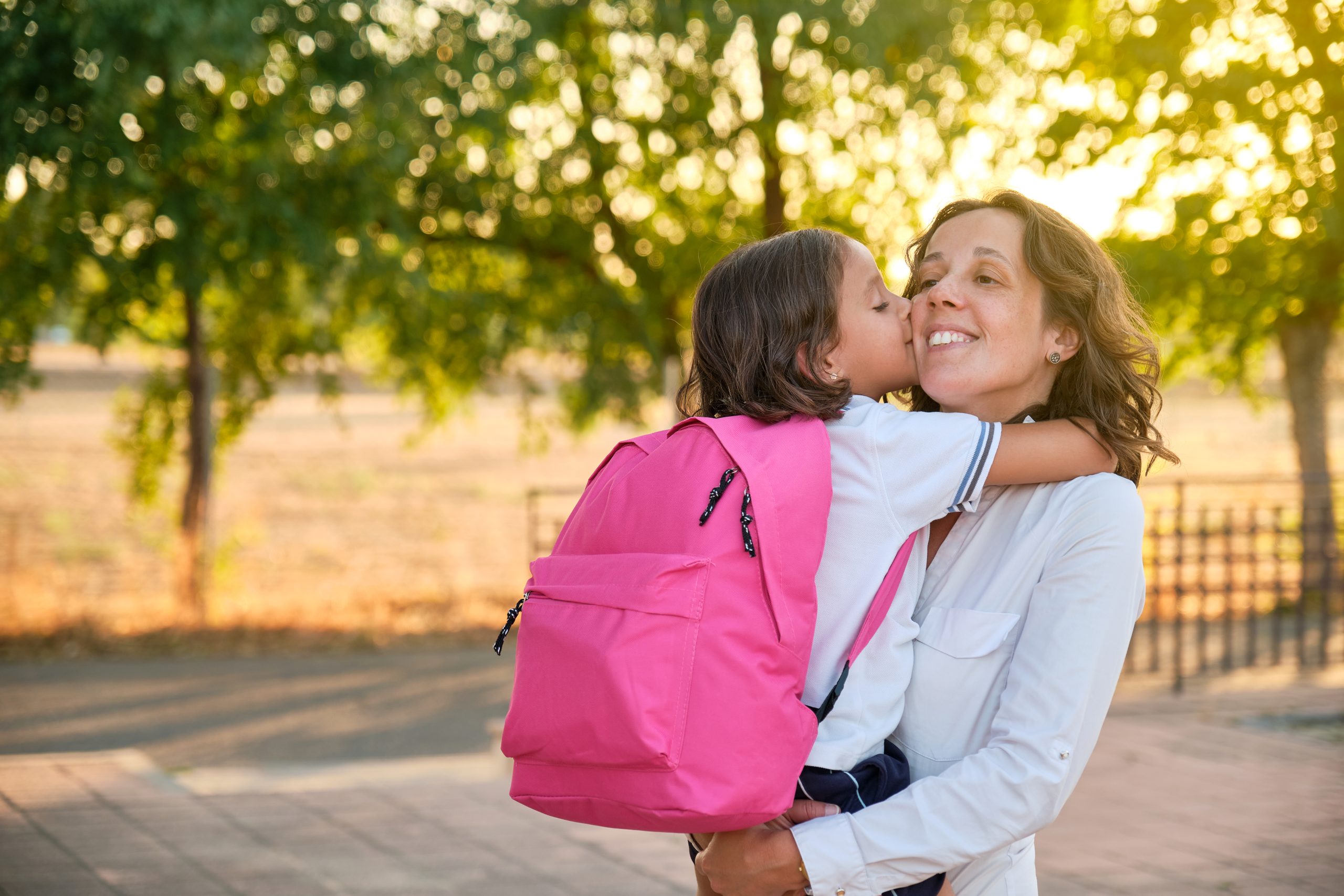 Madre abrazando a su hija con una mochila escolar rosa